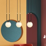 Lampa wisząca 3-punktowa Glam w kolorze czarnym i białym. Składa się z trzech okrągłych kloszy z białego szkła zawieszonych na czarnych kablach. Widoczna w aranżacji z kolorowymi ścianami w odcieniach żółci, niebieskiego i burgundowego.