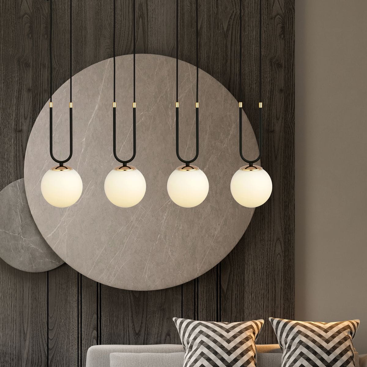 Czarna/biała lampa wisząca 4-punktowa Glam z czterema okrągłymi, mlecznymi kloszami zawieszonymi na cienkich, czarnych kabelkach. Lampa umieszczona na tle szarej, okrągłej dekoracji ściennej, z sofą i poduszkami w tle.