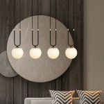 Czarna/biała lampa wisząca 4-punktowa Glam z czterema okrągłymi, mlecznymi kloszami zawieszonymi na cienkich, czarnych kabelkach. Lampa umieszczona na tle szarej, okrągłej dekoracji ściennej, z sofą i poduszkami w tle.