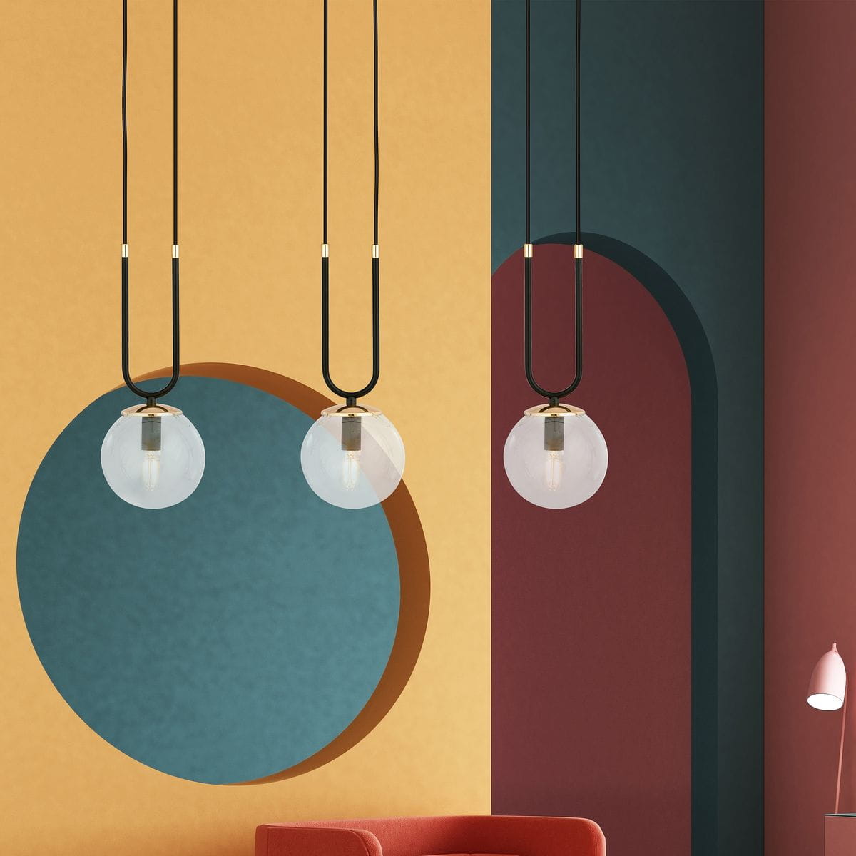 Czarna lampa wisząca 3-punktowa z transparentnymi kulistymi kloszami, zawieszona na długich czarnych przewodach. W tle kolorowa ściana z geometrycznymi wzorami w odcieniach żółtego, niebieskiego i burgundowego, w aranżacji z czerwonym sofą.