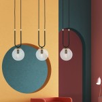 Czarna lampa wisząca 3-punktowa z transparentnymi kulistymi kloszami, zawieszona na długich czarnych przewodach. W tle kolorowa ściana z geometrycznymi wzorami w odcieniach żółtego, niebieskiego i burgundowego, w aranżacji z czerwonym sofą.