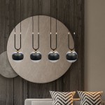 Czarna lampa wisząca Glam 4-punktowa z kulistymi kloszami, zawieszona na długich czarnych przewodach. Klosze mają złote detale i półprzezroczysty design. Umieszczona na tle jasnej ściany z okrągłym akcentem oraz poduszkami w geometryczny wzór.