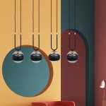 Czarna lampa wisząca 4-punktowa Glam z przezroczystymi kulami, zawieszona na długich czarnych przewodach, z elementami złotymi. Produkt w nowoczesnym wnętrzu, na tle kolorowych ścian w odcieniach zieleni, pomarańczy i czerwieni.