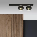 Fit lampa sufitowa 2-punktowa w kolorze czarnym, z metalowym stelażem i szklanymi kloszami. Zawieszona poziomo, z widocznymi żarówkami, na tle drewnianej struktury i gładkiej czarnej ściany. Idealna do nowoczesnych wnętrz.