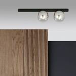 Lampa sufitowa 2-punktowa w kolorze czarnym i grafitowym z dwoma okrągłymi, metalicznymi kloszami. Ujęcie z góry, produkt zamontowany na suficie. W tle widoczne drewniane panele oraz czarna ściana.