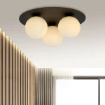 Czarna sufitowa lampa 3-punktowa z białymi, okrągłymi kloszami, zamontowana na gładkiej, okrągłej podstawie. Widok z dołu, w nowoczesnym wnętrzu z drewnianą ścianą i dużym oknem.