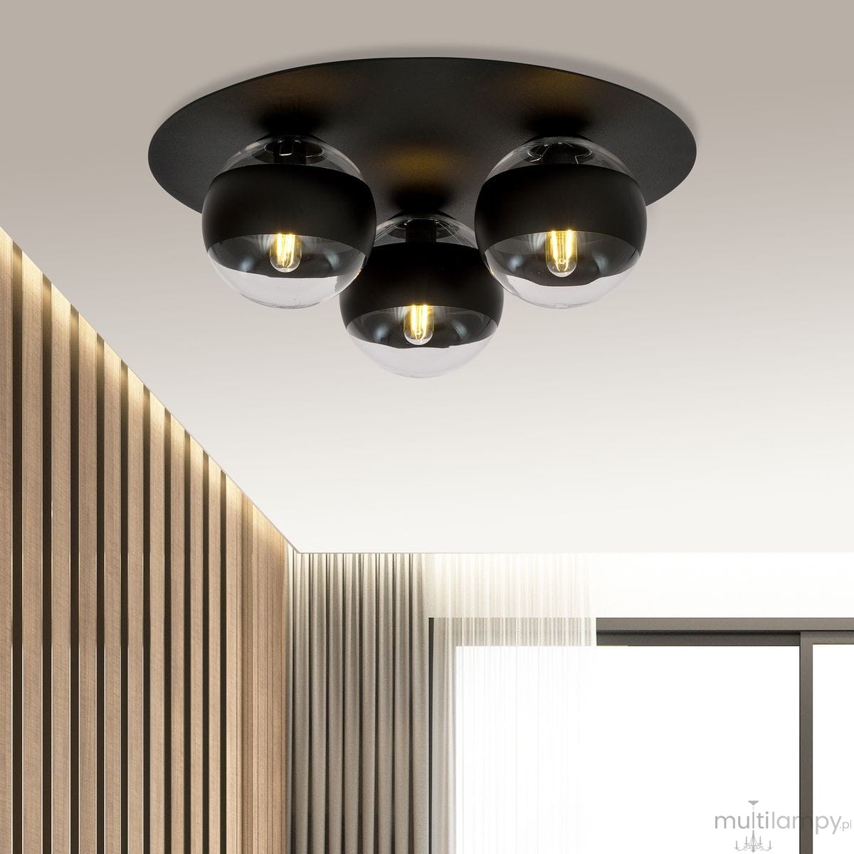 Czarna lampa sufitowa 3-punktowa z okrągłymi kloszami, z przezroczystymi elementami, zawieszona na okrągłej podstawie. Klosze mają widoczne żarówki, a tło to gładki sufit. Lampa pasuje do nowoczesnych wnętrz.
