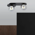 Czarna lampa sufitowa Plaza 2-punktowa z grafitowym mocowaniem, z dwoma okrągłymi, przezroczystymi kloszami. Produkt montowany na suficie, z widocznymi żarówkami, na tle szarym i czarnym. Idealna do nowoczesnych wnętrz.