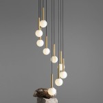 Lampa wisząca Riu 9-punktowa w kolorze czarnym i mosiężnym. Zawiera dziewięć białych, okrągłych kloszy zawieszonych na cienkich, czarnych linkach. Ujęcie z boku, lampa wisząca nad kamiennym podestem, z jednolitym szarym tłem.