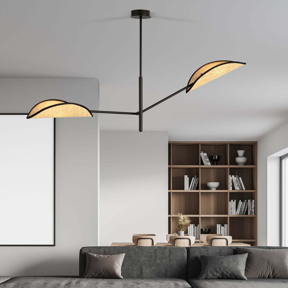 Lampa sufitowa Vene 2-punktowa w kolorze czarnym z rattanowym abażurem, wisząca, z trzema ramionami, umieszczona w nowoczesnym wnętrzu z szarym sofą i drewnianym regałem. W tle widoczny pusty obraz oraz dekoracyjne akcesoria.