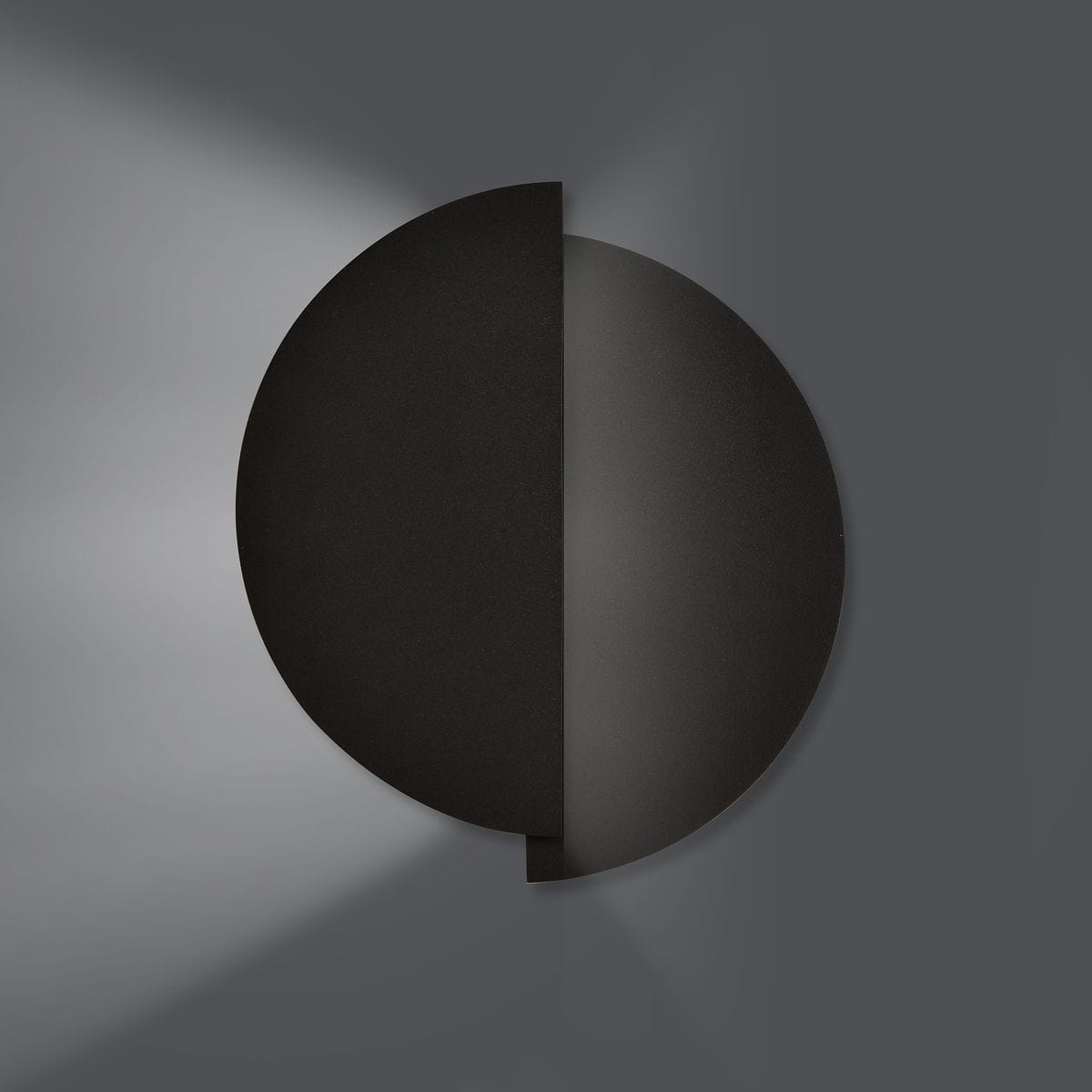 Kinkiet 2-punktowy Form 9 w kolorze czarnym o okrągłym kształcie, zamontowany na ścianie. Z jednej strony matowa powierzchnia, z której wydobywa się światło. W tle szare, minimalistyczne otoczenie.
