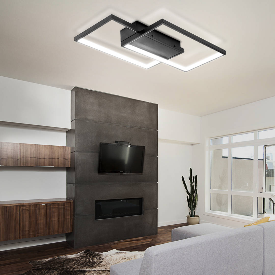 Kwadratowa lampa sufitowa LED 48W w kolorze czarnym, z dwiema punktami świetlnymi, zamontowana na suficie. W zestawie pilot do sterowania. Produkt umieszczony w nowoczesnym wnętrzu z telewizorem i rośliną.