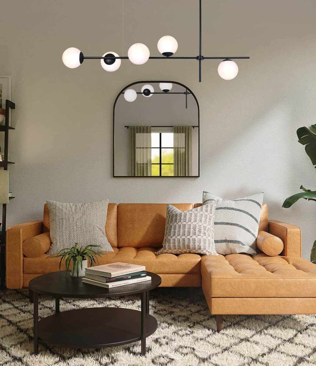 Lampa wisząca Vuelta 5-punktowa w kolorze czarnym, z białymi kulistymi kloszami, zawieszona nad brązową sofą w nowoczesnym wnętrzu. Lampa ma minimalistyczny design, idealna do salonu, z widocznym odbiciem w lustrze.