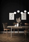 Lampa wisząca Camina 5-punktowa w kolorze czarnym, z pięcioma okrągłymi kloszami w białym kolorze, zawieszona w poziomie nad drewnianym stołem. Tło w ciemnym kolorze, z dekoracjami ściennymi i roślinnymi na stole, tworzy nowoczesną aranżację wnętrza.