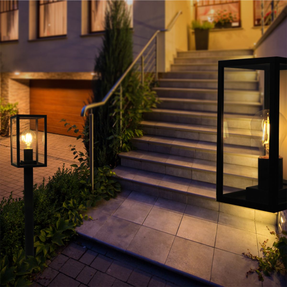 Lampa stojąca ogrodowa Malmo H68 w kolorze grafitowym, z prostokątną osłoną na żarówkę, umieszczona obok schodów. Produkt podświetla otoczenie, otoczony zielenią, w eleganckim, nowoczesnym stylu.