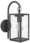 Malmo kinkiet elewacyjny ścienny 1-punktowy w kolorze grafitowym, wykonany z metalu z przezroczystym kloszem. Ujęcie z boku, prezentujące prostokątną formę z widoczną żarówką wewnątrz. Stojący na ścianie, z eleganckim, zakrzywionym mocowaniem.