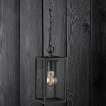 Malmo lampa wisząca ogrodowa 1-punktowa w kolorze grafitowym, o prostokątnej formie z metalowym stelażem i przezroczystymi ściankami. Zawieszona na łańcuszku, z widoczną żarówką w środku, na tle drewnianej ściany.