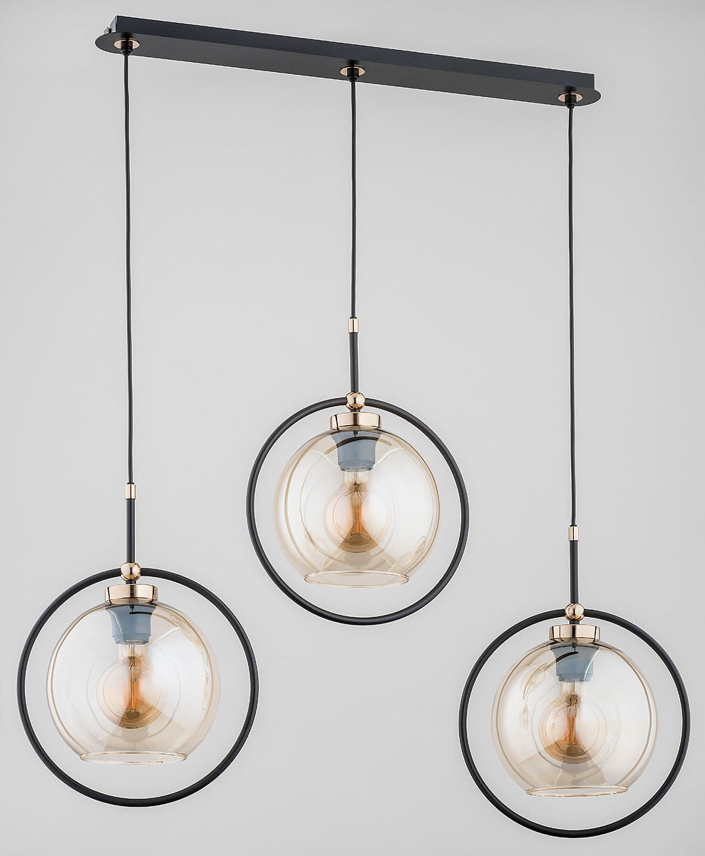 Lampa wisząca Seldi 3-punktowa z czarnym metalowym stelażem i złotymi akcentami. Trzy szklane klosze w kształcie kul, zawieszone na cienkich przewodach. W tle jasne, neutralne tło, co podkreśla elegancki design lampy.