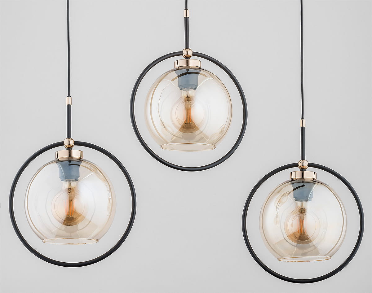 Lampa wisząca Seldi 3-punktowa w kolorze czarnym i złotym, składająca się z trzech szklanych kul w metalowych obręczach. Kule mają przezroczystą fakturę, a ich wnętrze oświetla żarówka. Produkt zawieszony na czarnych kablach, na jasnym tle.