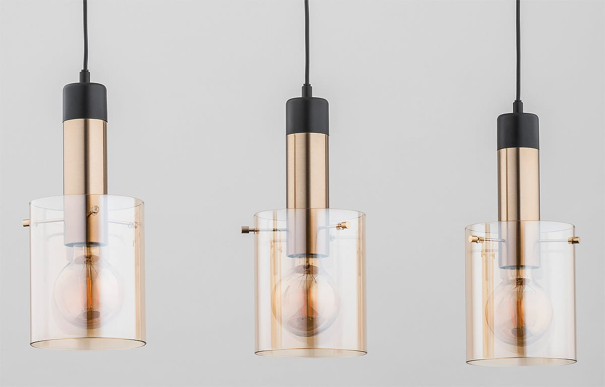 Lampa wisząca Bella 3-punktowa w kolorze złotym z przezroczystymi kloszami. Posiada trzy źródła światła, metalowe elementy w złotym odcieniu i czarne detale. Produkt zawieszony na cienkim przewodzie, z widocznymi żarówkami w kloszach.