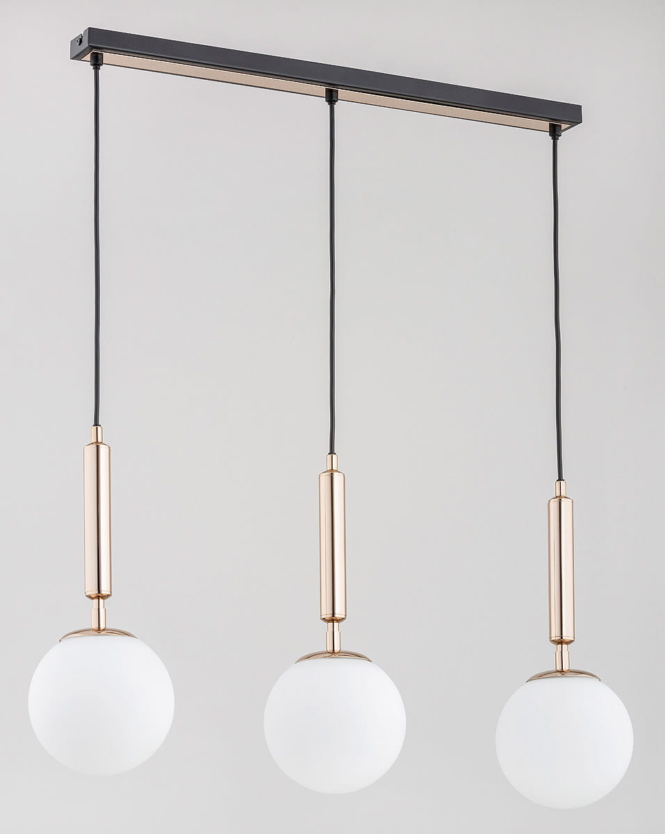 Lampa wisząca Volda Picolo White, 3-punktowa. Metalowy stelaż w kolorze czarnym z trzema kulistymi kloszami z matowego szkła. Każdy klosz zawieszony na złotej podstawie, w układzie równoległym, na ciemnym tle.