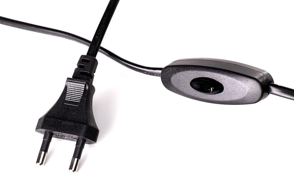 Zbliżenie na czarny kabel z wtyczką elektryczną oraz włącznikiem. Wtyczka ma dwa bolce, a włącznik jest prostokątny, z zaokrąglonymi krawędziami. Kabel jest gładki i elastyczny, co ułatwia jego układanie.