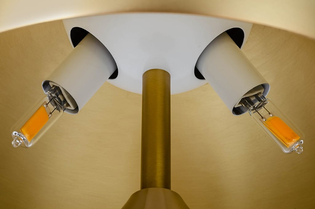 Lampa biurkowa Fungo 2-punktowa w kolorze złotym i mosiądzu. Widok z góry na dwa źródła światła w białych oprawach, z widocznymi żarówkami o pomarańczowym kolorze. Metalowa podstawa w złotym odcieniu.