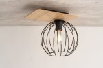 Czarna lampa sufitowa w kształcie kulistej klosza z metalowej siatki, zamontowana na prostokątnym drewnianym elemencie w kolorze dębu. Widoczna żarówka w środku. Ujęcie z dołu, na jednolitym jasnym tle.