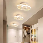 Biała lampa sufitowa 2-punktowa z okręgami LED o mocy 18W. Ujęcie z góry ukazuje trzy lampy zamontowane na suficie w nowoczesnym wnętrzu, z widocznymi elementami wystroju, takimi jak wieszaki na odzież i drzwi.