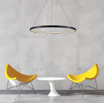 Lampa wisząca LED Ring D80, czarna, o okrągłym kształcie, zawieszona w centralnej części zdjęcia. Oświetlenie emituje ciepłe światło, a w tle widoczne są żółte krzesła i biały stół na szarej podłodze.