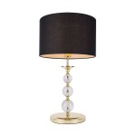 Lampa stołowa Rea II z czarnym abażurem i złotą podstawą. Wysoka, z przezroczystymi kulami na stelażu, umieszczona na okrągłej podstawie. Abażur w kształcie walca, wykończony od wewnątrz w jasnym kolorze.