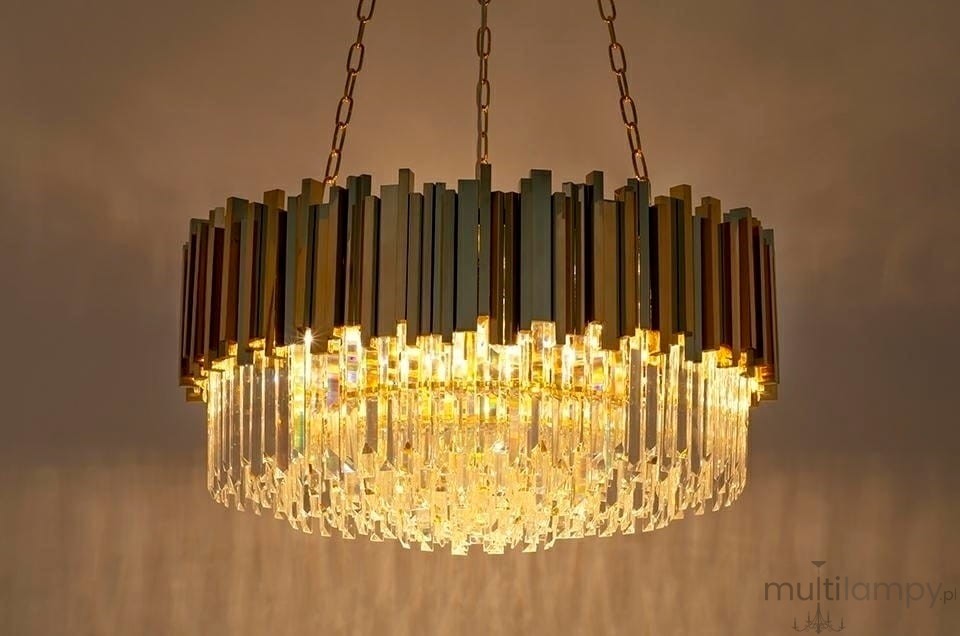 Lampa wisząca Imperial D80 w kolorze złotym, 16-punktowa, z przezroczystymi kryształkami. Kształt okrągły, z metalowymi elementami w pionowych pasach. Zawieszona na łańcuchu, emitująca ciepłe światło w eleganckim stylu.