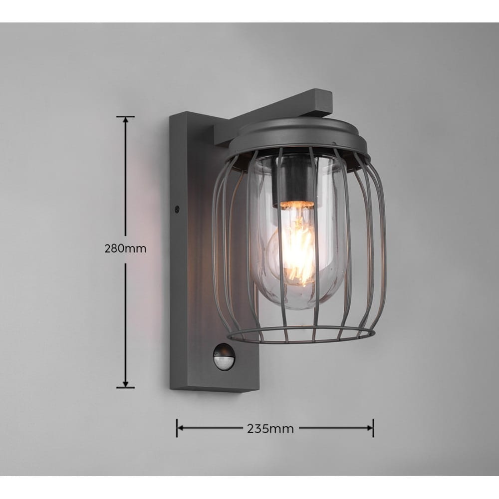 Kinkiet zewnętrzny Tuela w kolorze antracytowym, z czujnikiem ruchu. Oświetlenie w kształcie cylindrycznym, osłonięte metalową siatką, wymiary: 280 mm wysokości, 235 mm szerokości. Zainstalowany na ścianie, emitujący ciepłe światło.