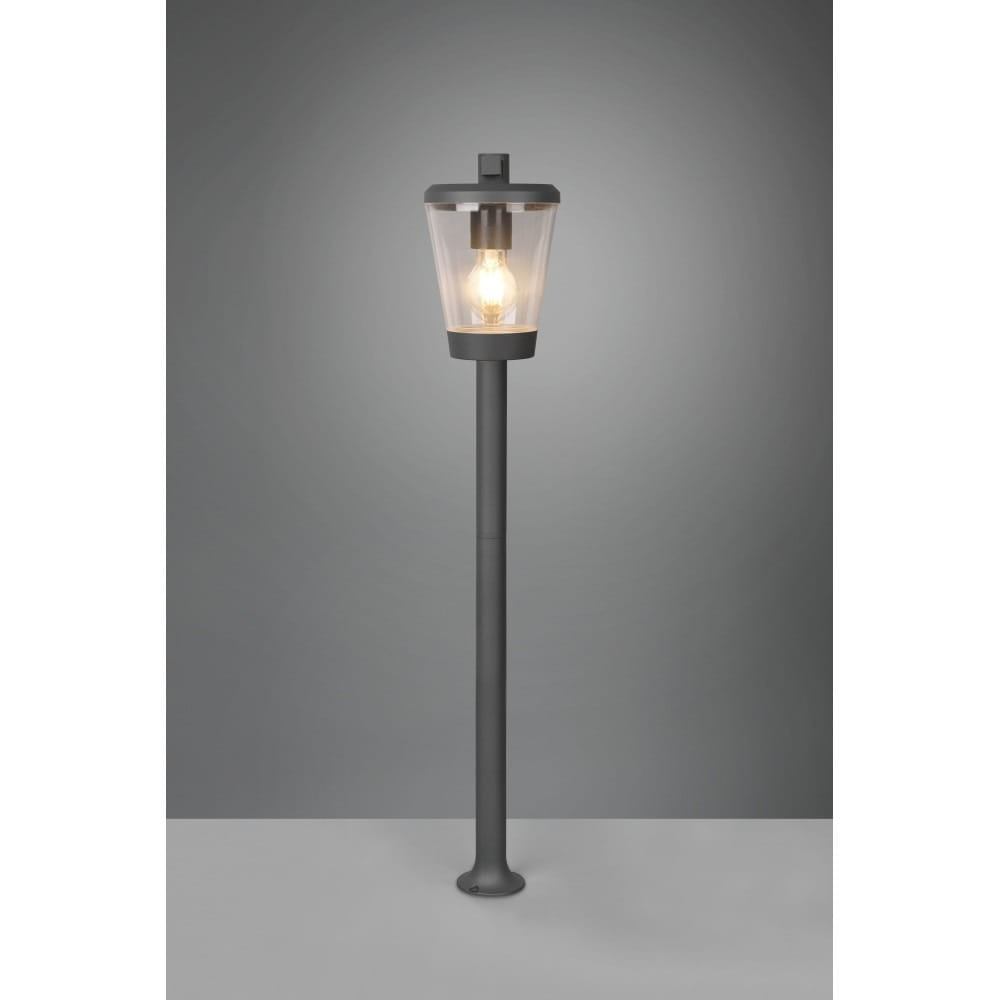 Stojąca lampa ogrodowa Cavado H100, antracytowa, z przezroczystym kloszem, na prostym słupku. Ujęcie frontalne, lampa włączona, emitująca ciepłe światło. Idealna do oświetlenia przestrzeni zewnętrznych.