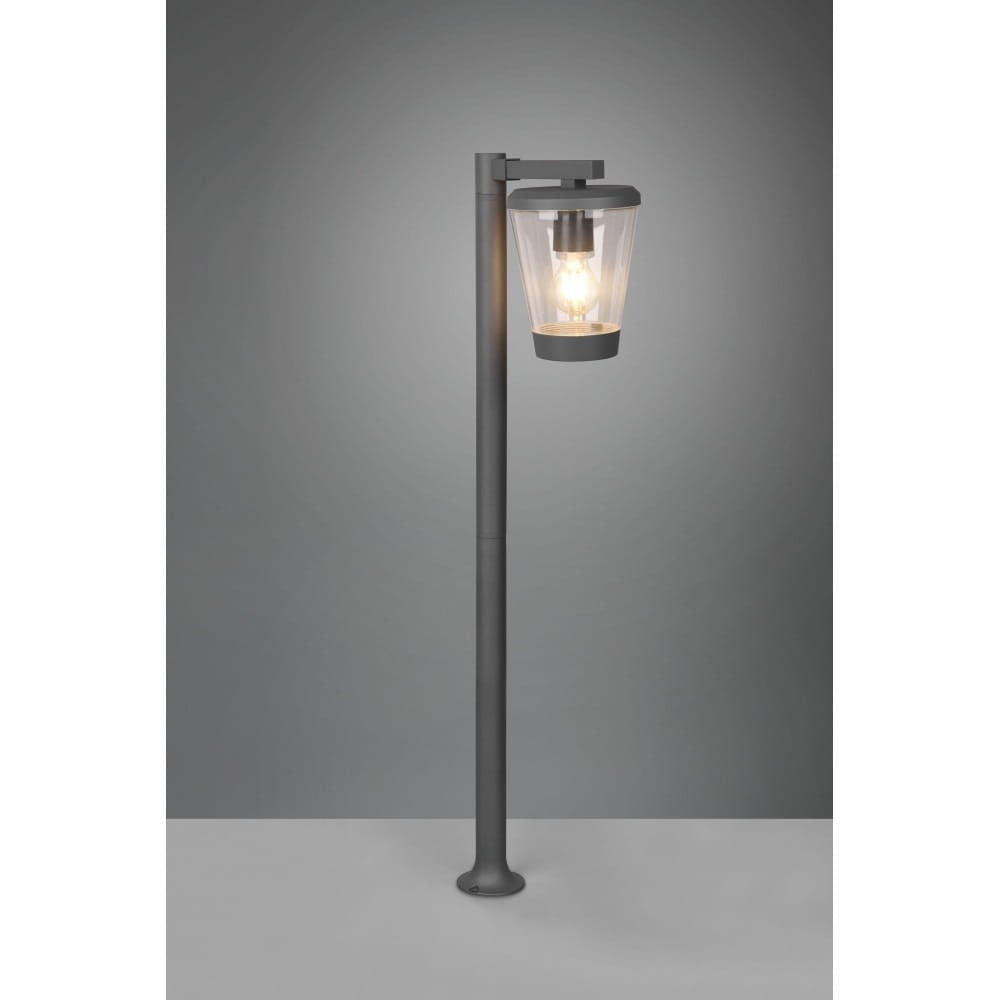 Lampa ogrodowa stojąca Cavado H100 w kolorze antracytowym, z przezroczystym kloszem, umieszczona na prostym słupku. Widok frontalny, oświetlona żarówka wewnątrz klosza. Tło w odcieniu szarości, podstawa stabilna.