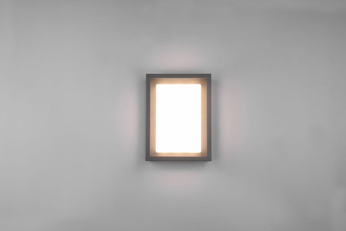 Kinkiet zewnętrzny Witham LED w kolorze antracytowym, o prostokątnym kształcie, zamontowany na ścianie. Emituje miękkie, ciepłe światło przez mleczną szybkę. Minimalistyczny design, idealny do nowoczesnych przestrzeni zewnętrznych.