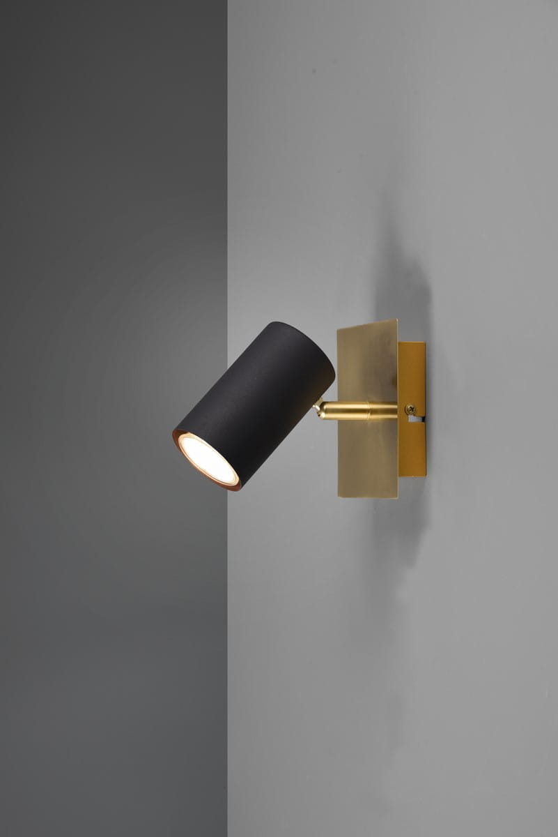 Czarny kinkiet Marley z metalowym, złotym wykończeniem, zamontowany na szarym tle. Lampa ma cylindryczny klosz, skierowany w dół, na prostokątnej podstawie. Styl minimalistyczny, idealny do nowoczesnych wnętrz.