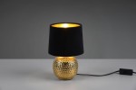 Lampa stołowa Sophia 1-punktowa z okrągłą, złotą podstawą o fakturze w drobne wgłębienia, pokryta czarnym abażurem. Ujęcie z boku, kabel z włącznikiem widoczny na stole. Tło szare.