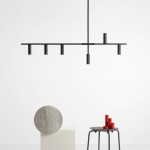 Lampa wisząca Trevo 6-punktowa w kolorze czarnym. Składa się z prostokątnego ramienia z sześcioma cylindrycznymi oprawami. Zawieszona na długim przewodzie, w minimalistycznym stylu. Tło białe, produkt znajduje się nad stołem z dekoracjami.