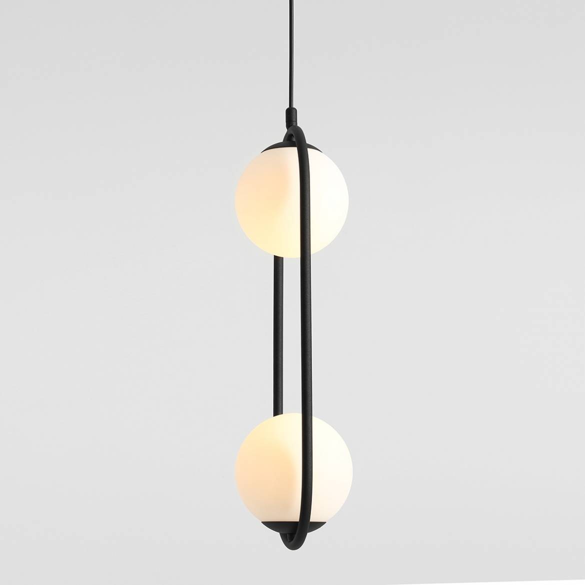 Czarna lampa wisząca Riva 2-punktowa, z dwoma okrągłymi kloszami z białego szkła, zawieszona na smukłym czarnym kablu. Klosze umieszczone są wzdłuż elastycznej, zakrzywionej oprawy. Tło jasnoszare.