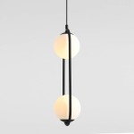 Czarna lampa wisząca Riva 2-punktowa, z dwoma okrągłymi kloszami z białego szkła, zawieszona na smukłym czarnym kablu. Klosze umieszczone są wzdłuż elastycznej, zakrzywionej oprawy. Tło jasnoszare.