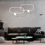 Czarna lampa wisząca Ovo LED 48W, złożona z dwóch okrągłych elementów, zawieszona nad sofą. Lampa emituje światło przez okrągłe źródło, tworząc nowoczesny efekt w aranżacji wnętrza. Tło to szara ściana i ciemne meble.