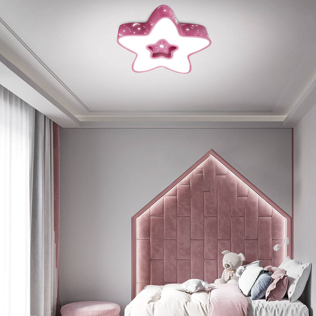 Różowa lampa sufitowa LED w kształcie gwiazdki z pilotem, zamontowana na suficie. Posiada dwa poziomy gwiazd, wykończona w błyszczącym materiale. Tło w jasnych odcieniach, z elementami dekoracyjnymi w pokoju dziecięcym.