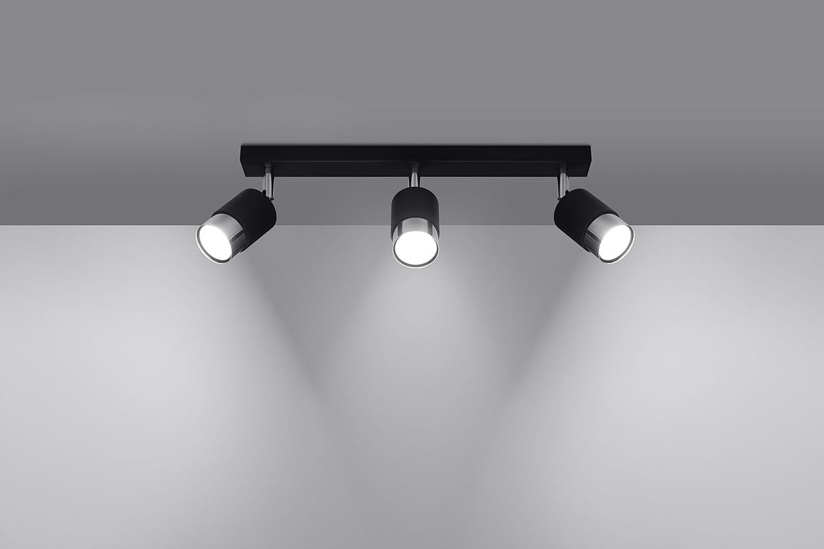 Czarna lampa sufitowa (spot) Nero z trzema punktami świetlnymi, umieszczona na prostokątnej chromowanej podstawie. Reflektory są ruchome, co pozwala na skierowanie światła w różne miejsca. Całość montowana do sufitu, w minimalistycznym stylu.