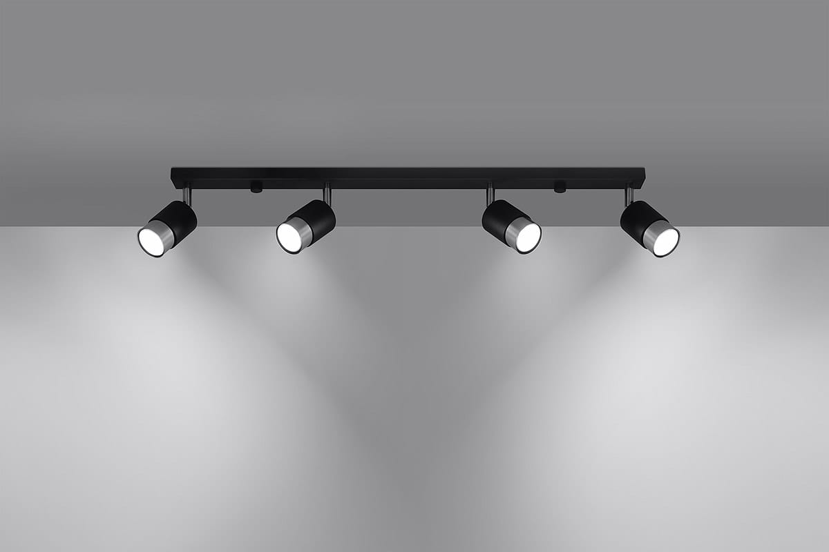 Czarna lampa sufitowa z czterema punktami świetlnymi, umieszczona na prostokątnej, chromowanej podstawie. Reflektory w formie cylindrów skierowane w dół, montowane na stropie. Tło w odcieniach szarości.