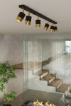 Lampa sufitowa Nero z sześcioma punktami świetlnymi, czarna z złotymi akcentami, zamontowana na prostokątnej podstawie. Widok z góry; elegancka forma idealna do nowoczesnych wnętrz. Tło w jasnych kolorach z elementami szklanymi i roślinnością.