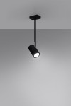 Czarna lampa sufitowa Norano, 1-punktowa, w formie cylindrycznego spotu. Ujęcie frontalne, zawieszona na prostym metalowym uchwycie. Emituje jasne światło, idealna do oświetlenia wnętrz. Tło w odcieniach szarości, minimalistyczna aranżacja.