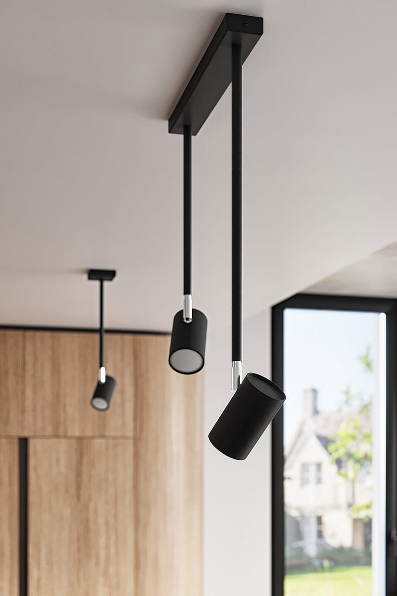 Jednopunktowa lampa sufitowa Norano w kolorze czarnym, zawieszona na prostokątnym uchwycie. Posiada dwa cylindryczne reflektory z matowej powierzchni, skierowane w różne strony, w nowoczesnym wnętrzu z widokiem na zewnątrz.