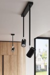 Jednopunktowa lampa sufitowa Norano w kolorze czarnym, zawieszona na prostokątnym uchwycie. Posiada dwa cylindryczne reflektory z matowej powierzchni, skierowane w różne strony, w nowoczesnym wnętrzu z widokiem na zewnątrz.