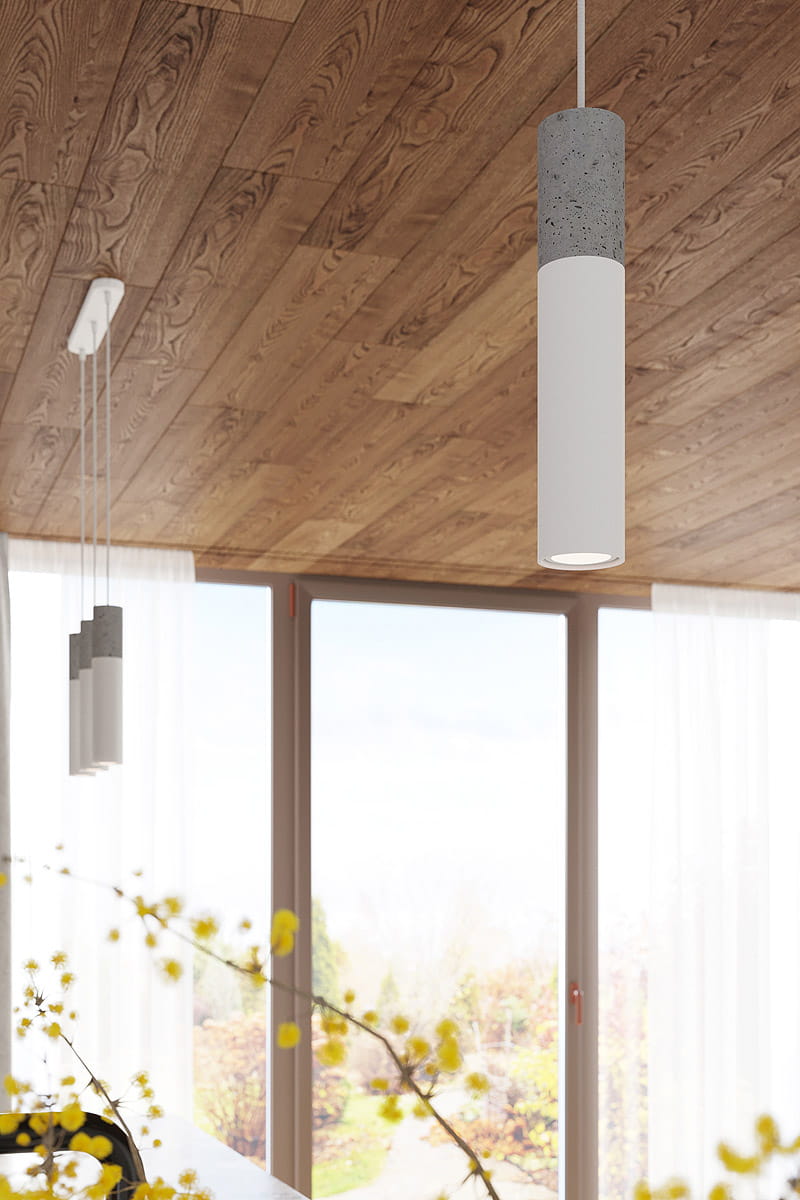 Lampa wisząca Borgio 1-punktowa w kolorze białym z szarym betonowym detalem, o cylindrycznym kształcie. Zawieszona na białym przewodzie, w tle widoczne okno z zasłonami. Idealna do nowoczesnych wnętrz.
